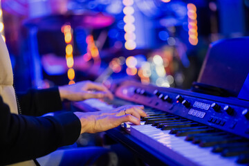 Musician pianist playing keyboard digital piano with blue blurred background with lights in concert