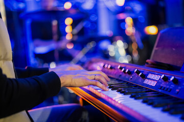 Musician pianist playing keyboard digital piano with blue blurred background with lights in concert