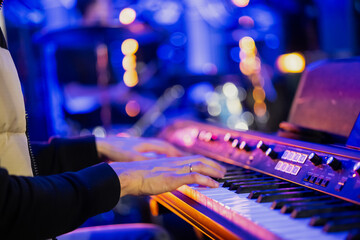 Musician pianist playing keyboard digital piano with blue blurred background with lights in concert