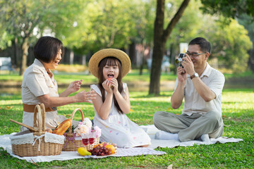 Happy family having picnic in the park with parents and kids sitting on the grass and enjoying...