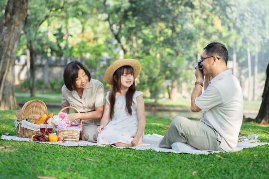 Happy family having picnic in the park with parents and kids sitting on the grass and enjoying taking a photo outdoors on a sunny summer day.