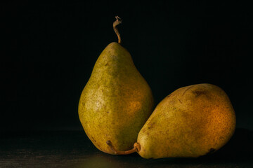 Two pears close-up on a black background. Bulk fruits. Photo in still life style.
