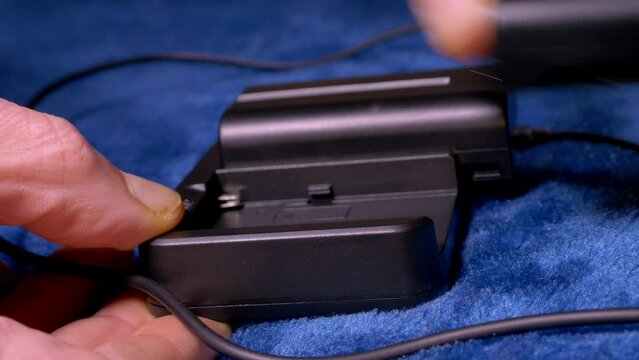 Closeup of a man's hands slotting two generic batteries - which could be for cameras, portable lights, etc - into a dual charger.