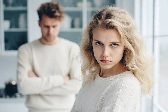 Upset young blonde woman and man argument, сlose up sad wife looks at camera in front and husband standing behind quarrel at home. Family conflict, crisis, psychological abuse, relationships concept