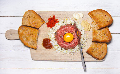 Tasty raw beef steak tartare with garlic, egg yolk, toasted bread, mustard, ketchup, peppers, onions and knife - a typical variant of Czech cuisine.