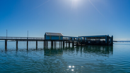 Victoria Point jetty and ferry terminal on a calm morning with sun star in the sky and on the water. Coochiemudlo Island in the distance. Queensland, Australia.