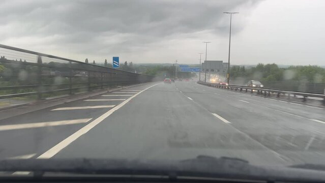 Car front view driving down the tallest bridge on Manchester ring road, the motorway M60 on overcast rainy day.