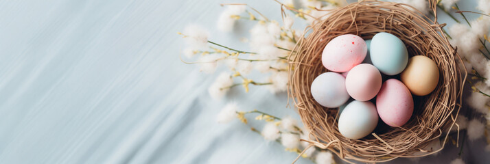 Fototapeta na wymiar Pastel Colored Easter Eggs in Bird's Nest on Blue Blurred Background with Cotton Branches. Easter Composition with Copy Space in Flat Lay Minimalist Style. Happy Easter Concept for Design, Banner.