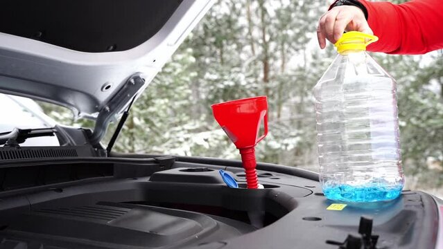 the driver pours winter windshield washer fluid into the car