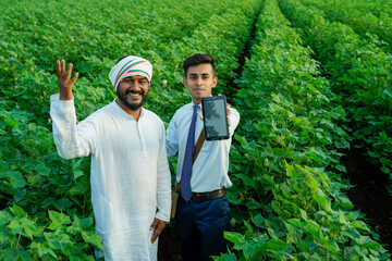 Young indian agronomist showing some information to farmer in tablet at agriculture field.