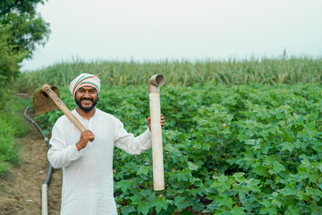 A young Indian farmer stands in the field, holding a shovel and a pipe