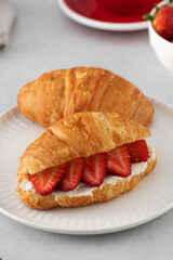 A fresh croissant with ricotta and fresh strawberries. Croissant with black coffee.