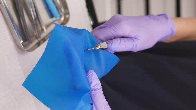 Preparing cofferdam for use. Dentist uses rubber dam system with latex scarves and pierces hole with special tool. Modern dentistry. Vertical video.