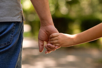 the father's hand held tightly the hand of his little son against the background of green foliage, close-up