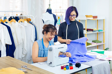 Team of fashionable freelance dressmaker sewing on  new custom made dress while working inside...