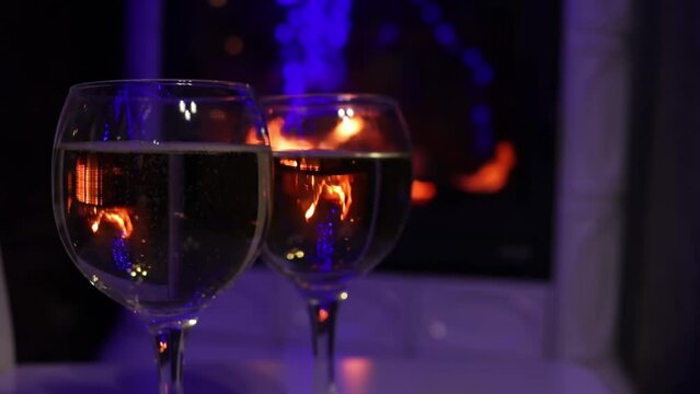 Closeup view of couple of champagne glasses nearby fire. Bubbles and fire reflections in wine glasses
