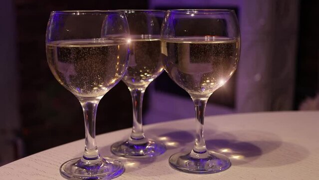 Three glasses of champagne standing near fireplace. Closeup view of wine glasses with bubbles in slow motion