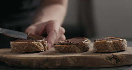 man spreading chocolate hazelnut spread on ciabatta slice on wood board