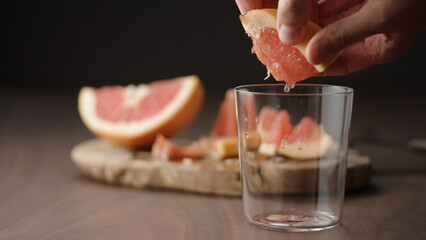 man squeeze grapefruit into tumbler glass on wood table