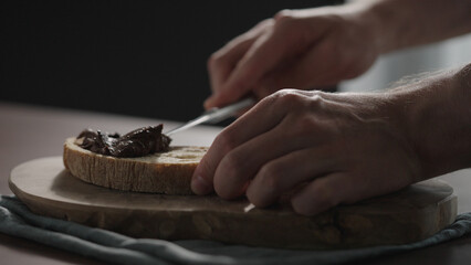 man spreading chocolate spread on ciabatta slice on olive board
