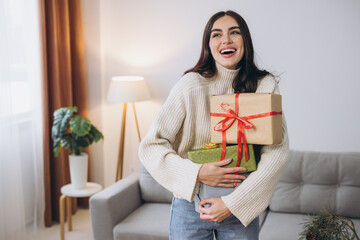 Beautiful happy woman is wrapping and holding Christmas presents at home