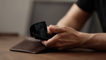 man cleaning leather wallet on wood table - obrazy, fototapety, plakaty