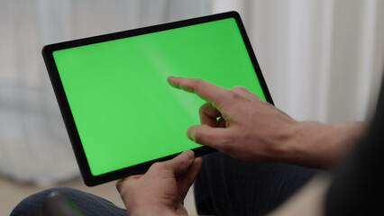 Man sitting indoors on a chair with tablet pc with green screen