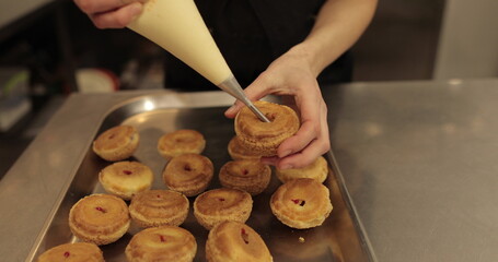 The confectioner fills the eclair with cream using a pastry syringe. Female hands with a cooking...