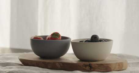 strawberries and blueberries in bowls on wood table