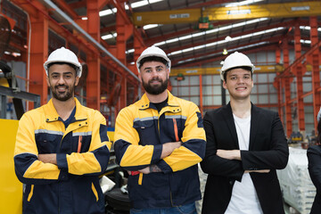 Group of male factory workers standing together with crossed arms and smiling in industry factory, wearing safety uniform and helmet. Factory workers working in factory