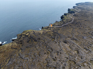 Volcanic rock formations on the coast in Iceland.There is an orange lighthouse