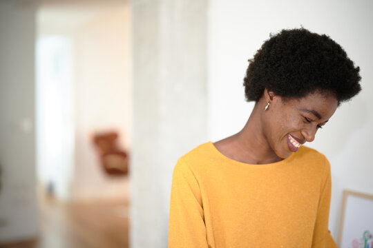 Portrait of a shy beautiful afro woman with acne smiling in the office looking down. Smiling woman enjoying a moment in a bright workspace. Joyful Moment at Work