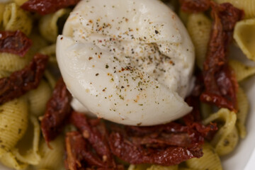 Closeup of pesto conchiglie with sundried tomatoes and burrata cheese served in blue bowl