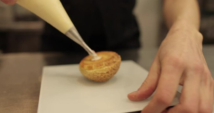 The confectioner fills the eclair with cream using a pastry syringe. Female hands with a cooking syringe close-up
