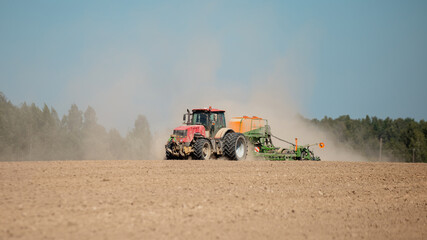 A powerful farm tractor with a mechanical plow raises dust on a hot day - machinery cultivates a...