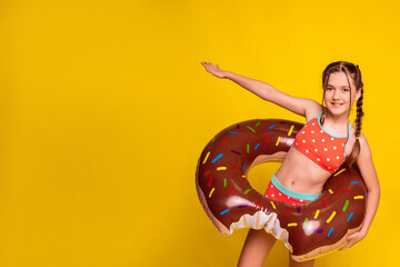 happy child girl want to swim holding inflatable ring on yellow studio background. banner with copy...