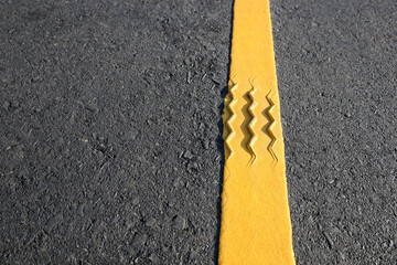 Tire marks on reflective yellow stripes. Close up bumps in traffic lines on black asphalt road...