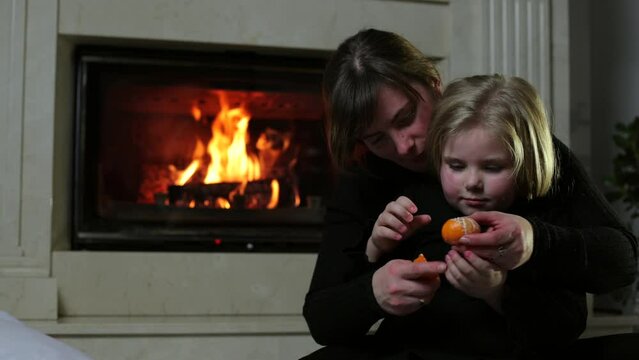 Family near the fireplace. Mother and daughter are sitting in the room, a fire is burning in the background, a hot fireplace. Cozy atmosphere, warm room in winter