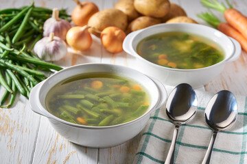 Green soup with potato, green bean and carrot on a white plate on wooden background.