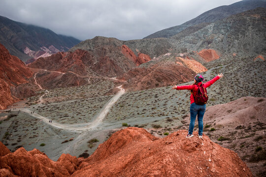 Mujer turista en la cima de un cerro colorado con los brazos abiertos en señal de felicidad, en Purmamarca, Jujuy	