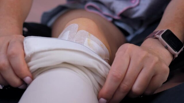 A woman lowers a compression stocking from her knee to perform a knee bandage.