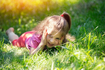 Happy little girl lying on the grass in the garden on a summer sunny day