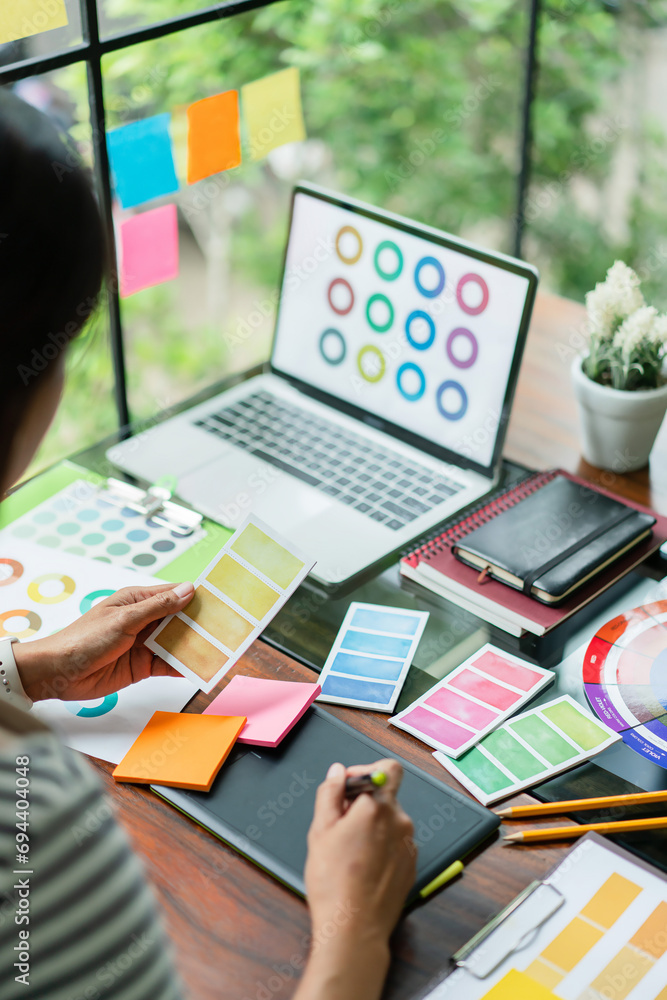 Poster creative graphic designer comparing color swatch on paper and laptop to designing project on tablet