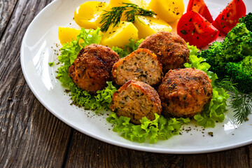 Fried pork meatballs with boiled potatoes and cooked broccoli on wooden table
