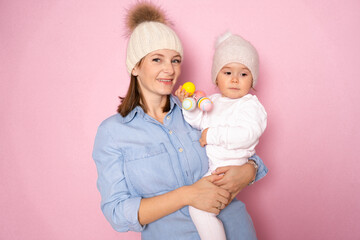 young woman and cute baby girl in winter woolen sweaters and hats isolated on pink background