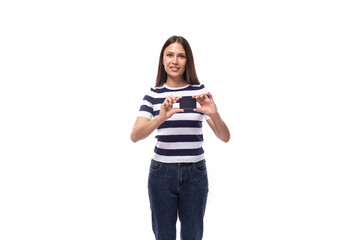 young brunette european lady of slim build dressed in a striped summer t-shirt holding a plastic bank card with a template