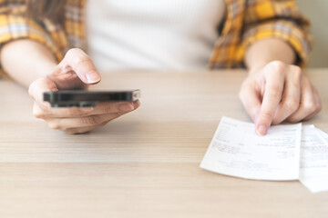 Bill pay concept. Online internet banking asian young woman hand holding receipt paper, using...