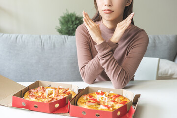 Diet concept, unhappy asian young woman, girl refusing to eat Pizza in box at home, hand pushing...