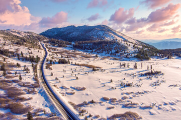 Aerial view of  a Sunrise over Mt. Rose located near Reno and Lake Tahoe Nevada with magenta clouds, snow capped mountains and a winding road in the snow towards the background.