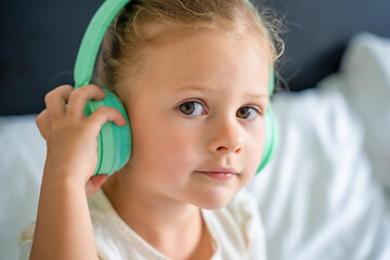Cute little girl enjoying music using green kids headphones in home bed
